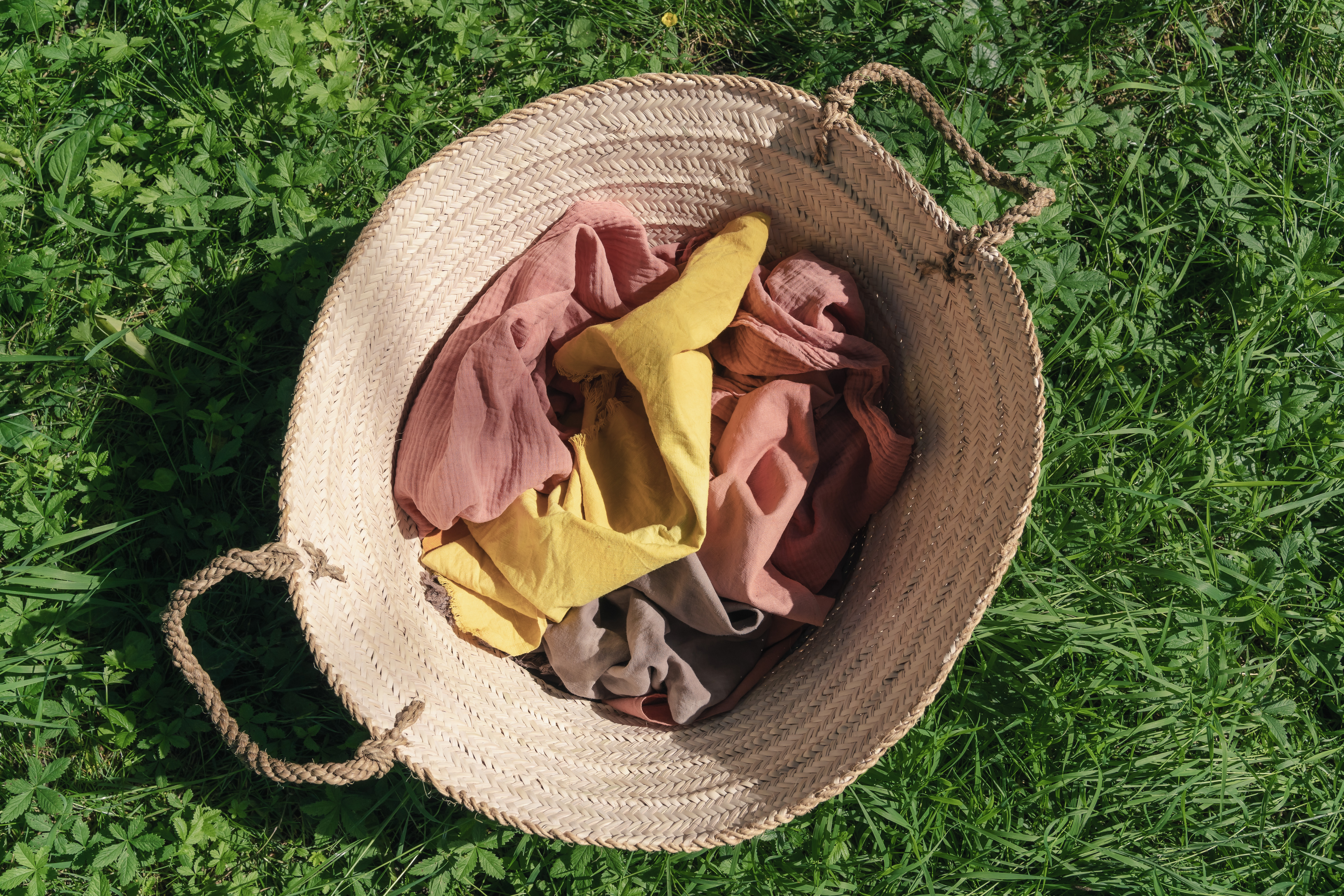 Woven straw basket with hand-dyed fabrics on green grass